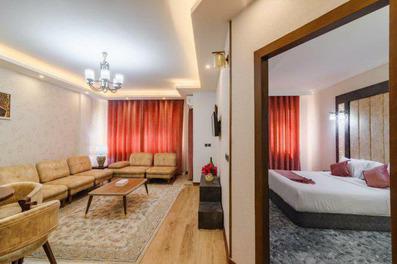 سوئیت یک خوابه هتل آرتمیس قشم با مبلمان کرم با کوسن های قرمز، لوستر، تابلو، فرش و پرده قرمز