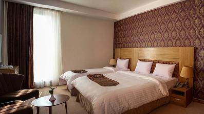 اتاق سه نفره در هتل؛ تخت دو نفره + تخت یکنفره با ملحفه سفید در آن دیده می شود.