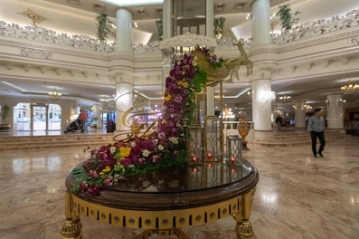 میز دایره ای طلایی رنگ با گل آرایی زیبا تزئین شده. میز در لابی هتل قصر طلایی مشهد با کف سنگی قرار گرفته است.