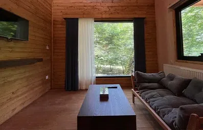 طبقه همکف کلبه چوبی دوتخته در هتل جنگلی میزبان با پنجره های سراسری بلند